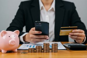 © Sultan - stock.adobe.com Mann mit Smartphone, Bankomatkarte, Sparschwein und Münzen